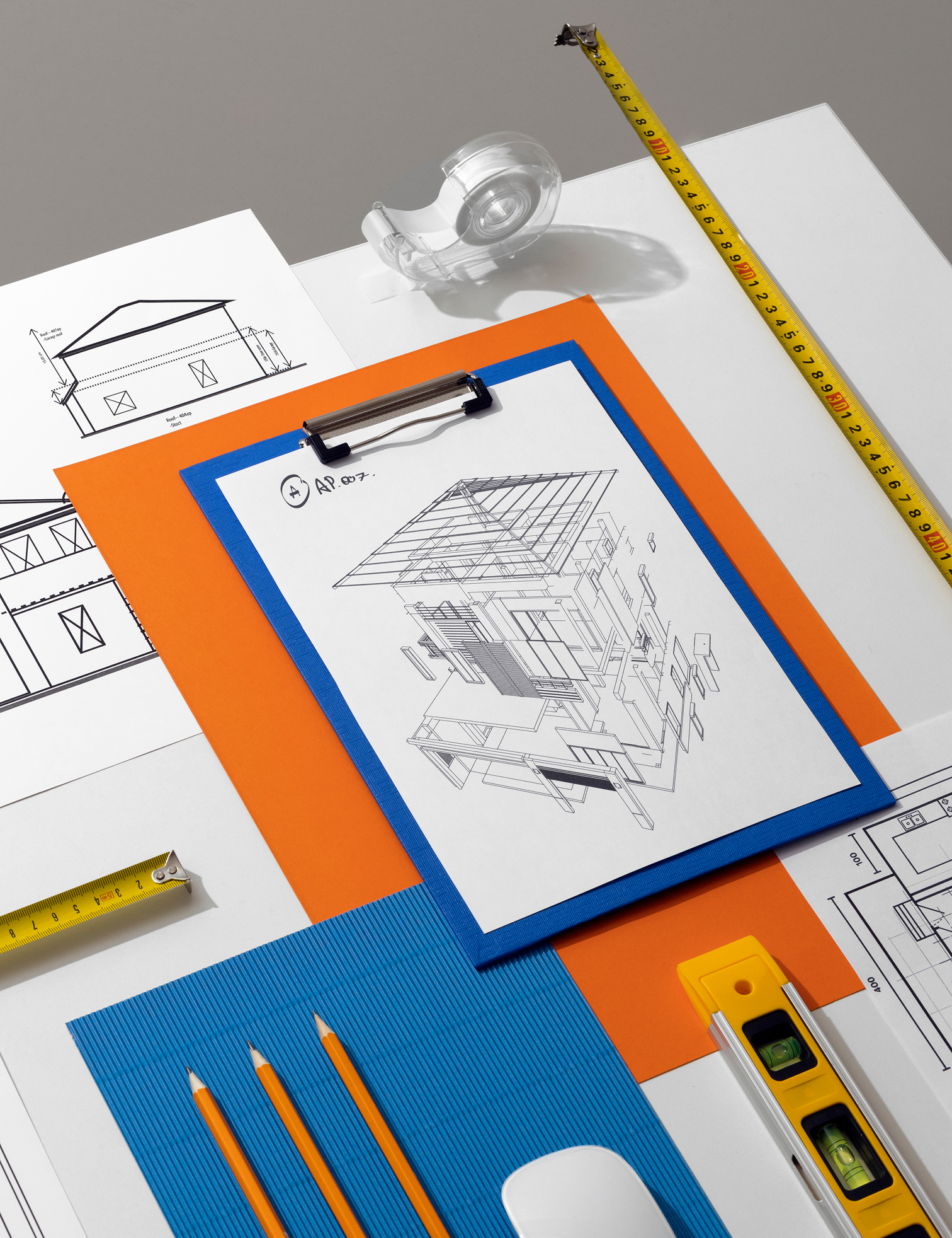 Progetti architettonici, metro a nastro e attrezzi sono stesi su una scrivania. AP.007.